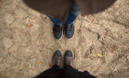 Man and woman stand opposite each other. Close up of feet in winter boots in the sandの写真素材