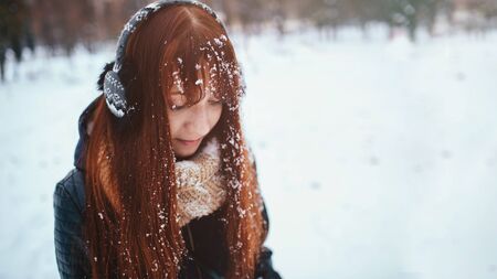 Winter. Woman with red hair wearing ear muffs . She is looking down. Snow on theの写真素材