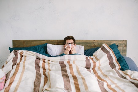 young man with handkerchief. Sick guy on the bed has runny nose. man makes a cure for the common...