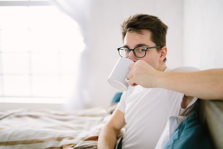 man in bed drinking morning coffee in sunrise lightの写真素材