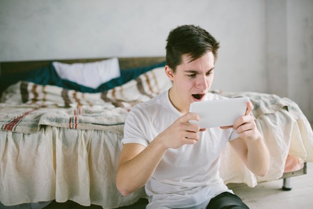 handsome man surfing on tablet. Guy talking with friends, video conference, skype, tablet. The young student scrolls social networksの写真素材