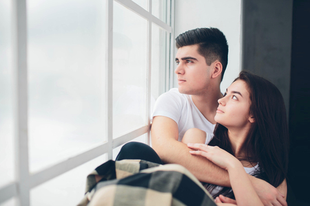 A loving couple are lying by a window bathed in sunlight. Bright and cozy bedroom. Family comfort and loveの写真素材