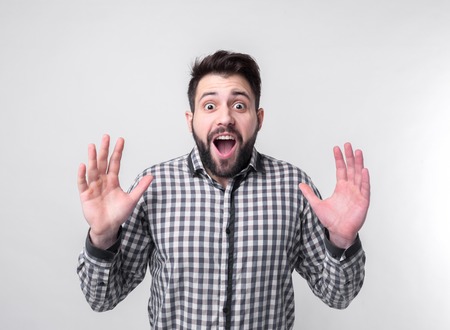 Young man with arms raised. Guy spread hands out. Isolated on white background. Bearded student wearing a white shirt arms opened looking up.の写真素材