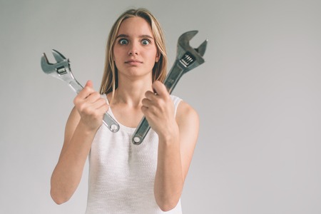 Funny portrait upset craftswoman. Blonde woman is wearing shirt isolated on white. Girl does not know how to use a drillの写真素材