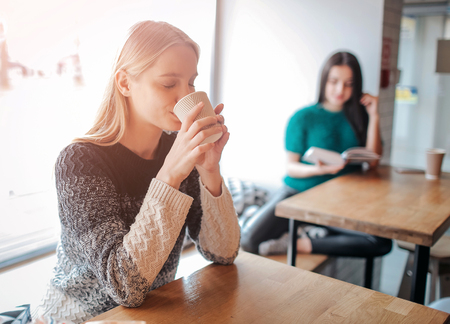 Young beautiful woman drinking coffee at cafe bar. Female model in the morning at restaurantの写真素材