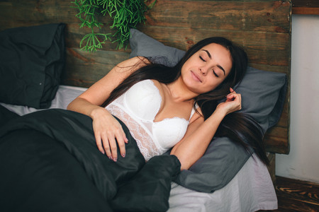 Side view of beautiful young woman smiling while sleeping in her bed at homeの写真素材