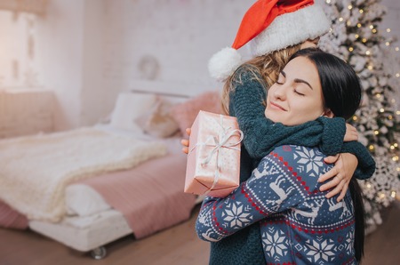 Merry Christmas and Happy Holidays Cheerful mom and her cute daughter girl exchanging gifts. Parent and little child having fun near Christmas tree indoors. Morning Xmas. Portrait family close upの写真素材