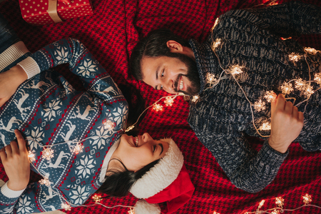 Merry Christmas and Happy New Year . Young couple celebrating holiday at home. Woman and man lie on the carpet and looking at each other. Top viewの写真素材