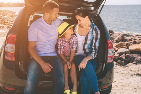 Happy family on a road trip in their car. Dad, mom and daughter are traveling by the sea or the ocean or the river. Summer ride by automobileの写真素材