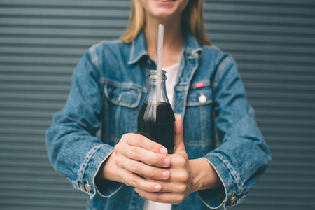 drinks, people and lifestyle concept - close up of happy woman drinking cola with straw near the gray wallの写真素材