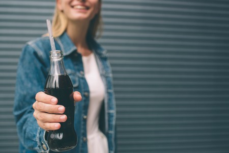 drinks, people and lifestyle concept - close up of happy woman drinking cola with straw near the gray wallの写真素材
