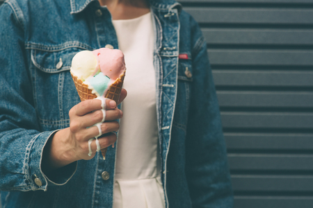 Portrait of young happy girl eating ice-cream, outdoor, over blue wall background.の写真素材
