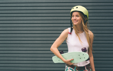 Young blonde woman with a skateboard in his hand against the background of a Striped wallの写真素材