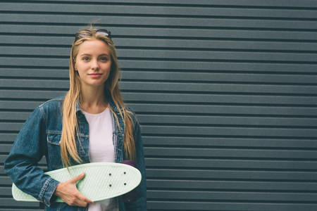 Young blonde woman with a skateboard in his hand against the background of a Striped wallの写真素材