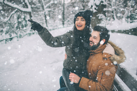 Happy Young Couple in Winter . Family Outdoors. man and woman looking upwards and laughing. Love, fun, season and people - walking in winter park. Female model sits on his lap.の写真素材