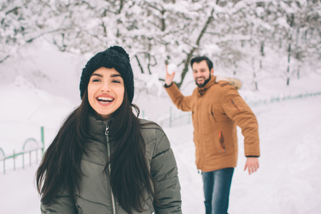 Happy Young Couple in Winter . Family Outdoors. man and woman looking upwards and laughing. Love, fun, season and people - walking in winter park. He is snowballingの写真素材
