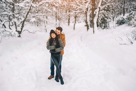 Happy Young Couple in Winter . Family Outdoors. man and woman looking upwards and laughing. Love, fun, season and people - walking in winter park. Its snowing, theyre huggingの写真素材