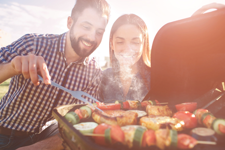 Friends making barbecue and having lunch in the nature. Couple having fun while eating and drinking at a pic-nic - Happy people at bbq party.の写真素材