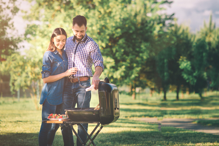Friends making barbecue and having lunch in the nature. Couple having fun while eating and drinking at a pic-nic - Happy people at bbq party.の写真素材