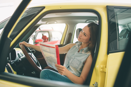 Beautiful young woman buying a car at dealership. Female model sitting in the car interiorの写真素材