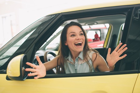 Beautiful young woman buying a car at dealership. Female model sitting in the car interior