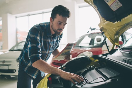 Perfect lines. The young dark-haired bearded man examining car at the dealership and making his...