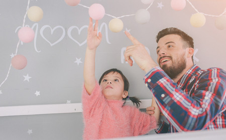 Cute little daughter and her handsome young dad iare playing together in childs room. Dady and child spend time together while sitting on the floor in bedroomの写真素材