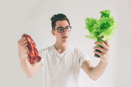 Vegetarian concept. Man offering a choice of meat or vegetables Salad leaves . Nerd is wearing glasses.の写真素材