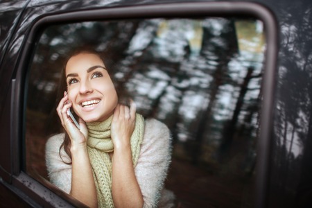 Beautiful woman smiling while sitting on the passenger seats in the car. Girl is using a smartphoneの写真素材