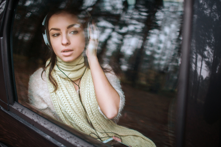 Woman in the car, autumn concept. Smiling pretty girl listening to music with headphones moving in...