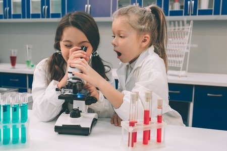 Two little kids in lab coat learning chemistry in school laboratory. Young scientists in protective glasses making experiment in lab or chemical cabinet. Looking through the microscopeの写真素材