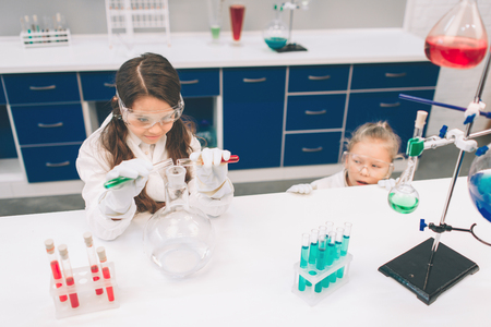 Two little kids in lab coat learning chemistry in school laboratory. Young scientists in protective glasses making experiment in lab or chemical cabinet. Studying ingredients for experiments .の写真素材