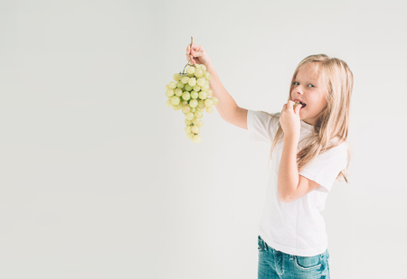 Girl holding grape, close up. concept. isolated on white. Nerd is wearing glasses. Child isolated on white background.の写真素材