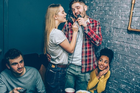 Boy and girl standing in the middle of the room, holding two microphones and singing together very well.の写真素材