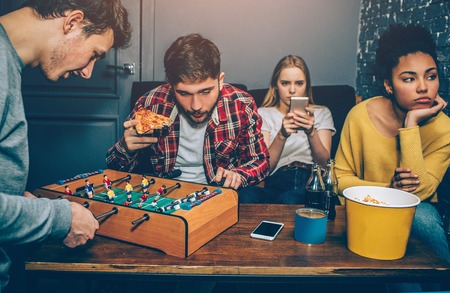 Two boys are playing board football game. They are very concentrated on it while girls are watching...
