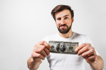Close up of handsome brunette man standing near the white wall and holding a dollar bill.の写真素材
