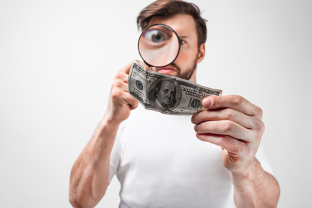 Cut view of a young man that holds a hundred dollar bill and looking on it through the loupe.の写真素材