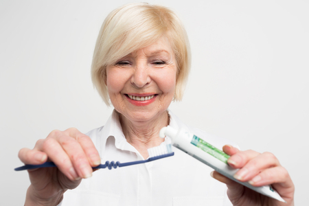 Close up and cut vuew of a woman putting some toothpaste on the toothbrush. She wants to clean her teeth. The lady is having some care about her mouth. Isolated on white background.の写真素材