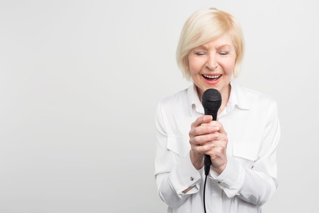 Beautiful and tender picture of awesome mature woman singing a song with her eyes closed using a microphone. Isolated on white background.の写真素材