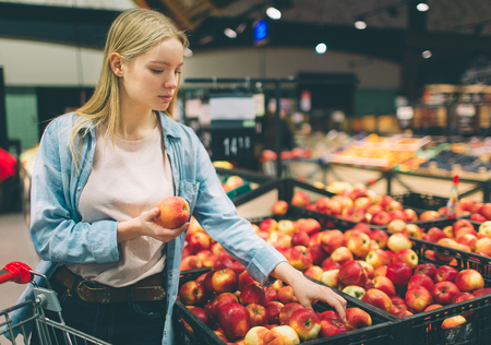 Nice and attractive youn woman is taking some apples at the store. She is choosing the best one.の写真素材