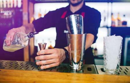 Close up of barman adding some alcohol into the small cup and holding it. There are two cups standing one on another at the barmans stand.の写真素材