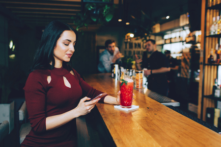 Nice picture of beautiful girl sitting at the barmans stand in the club and looking to the phone....