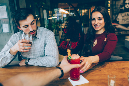 A picture of girl getting a cocktail from the barman. Guy is sitting besides her and drinking his drink. Also he is looking to the girl. Young woman looks happy and satisfied.の写真素材
