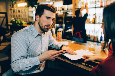 A business meeting of two people in a bar. Man is explaining something to woman. She is listening to him very accurate and careful. Barman is standing not far from them.の写真素材