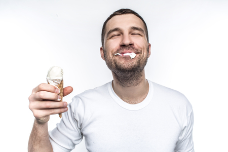 Cheerful and joyful man is eating an ice cream not very accurate but with big pleasure. Isolated on white background.の写真素材
