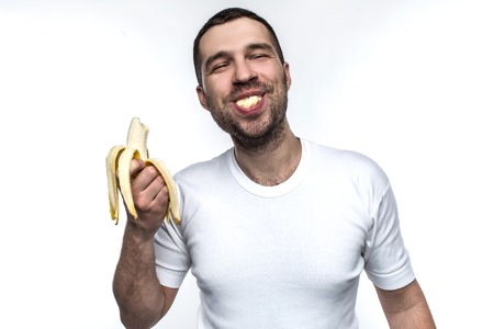 Funny and strange man is eating banana. He is enjoying that. Man is eating banana in a funny manner. His behave is like a small boy has. Isolated on white background.の写真素材