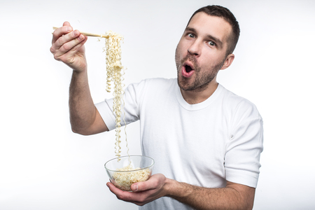 A picture of guy that likes to eat oriental cuisine. He has a plate of thai spaghetti and keep it with special sticks for food. Also this weird guy likes to eat junk food. Isolated on white background.の写真素材