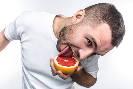 Hilarious picture of guy in white shirt licking the half of the grapefruit. He is looking to the...