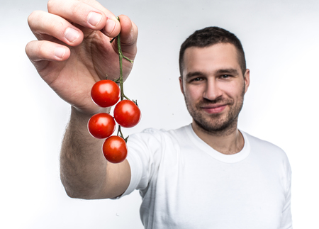 Attractive and handsome man is holding a ramus of cherie tomatoes. This vegane likes to eat every fruit and vegetable in a world. He recommends to eat only good food. Isolated on white background.の写真素材