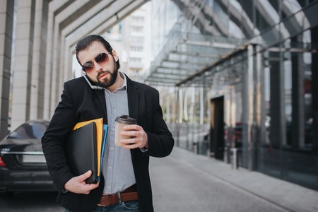 Busy man is in a hurry, he does not have time, he is going to eat snack on the go. Worker eating, drinking coffee, talking on the phone, at the same time. Businessman doing multiple tasks. Multitasking business person.の写真素材